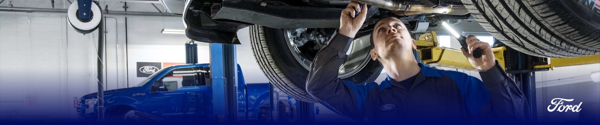 A Ford Service Technician inspecting the underside of a Ford vehicle on a lift in a clean, bright service center.