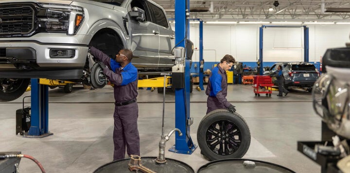 Ford technicians service vehicles in a professional dealership bay, removing a truck wheel and inspecting cars on lifts.